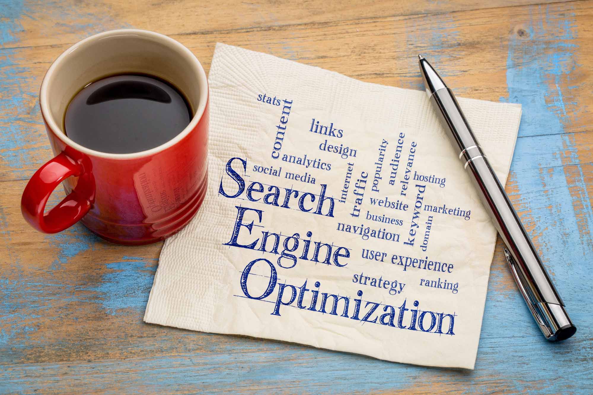 Napkin with words related to search engine optimization written on it surrounded by coffee cup and pen